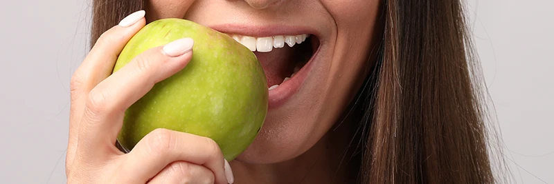 Junge Frau mit grünem Apfel auf grauem Hintergrund